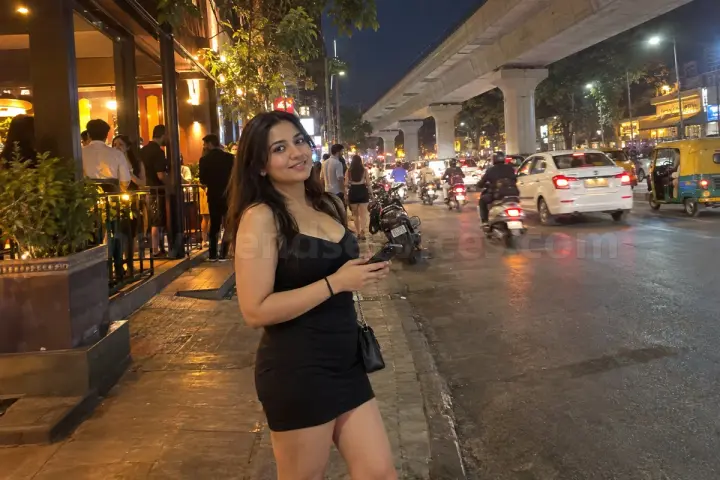 Woman in a black dress outside a pub on 100 Feet Road, Indiranagar, with the metro line above