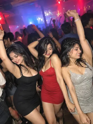 Three girls in party dresses dancing in a crowded Bangalore pub