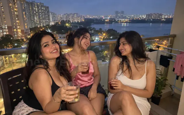 Three girlfriends with drinks on a flat balcony facing Bellandur lake