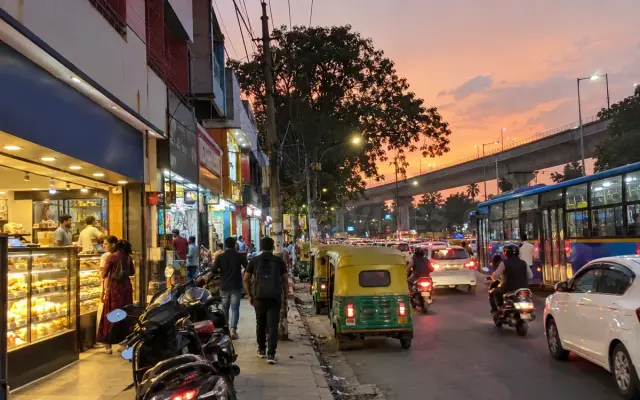 Banaswadi Main Road at sunset with shops, autos and a city bus