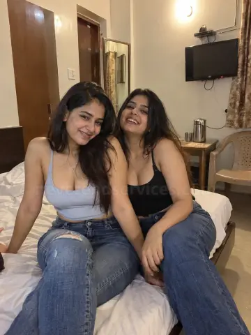 Two girls in jeans sitting on a bed in a budget lodge room