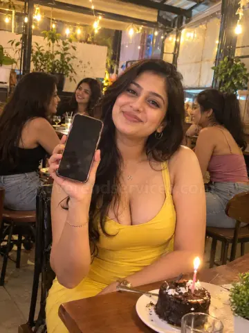 Smiling woman in a yellow dress holding up her phone at a cafe