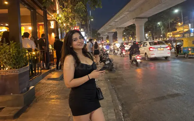 Woman in a black dress outside a pub on 100 Feet Road, Indiranagar, with the metro line above